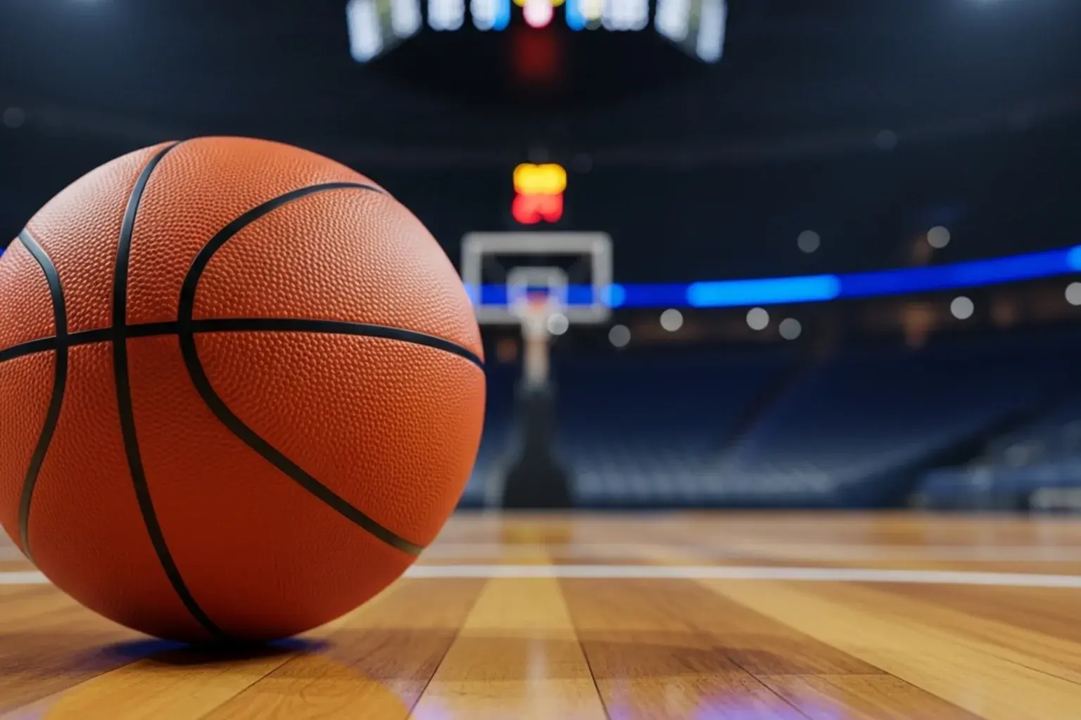 Close-up of a basketball on a polished hardwood court with arena scoreboard glowing in the background